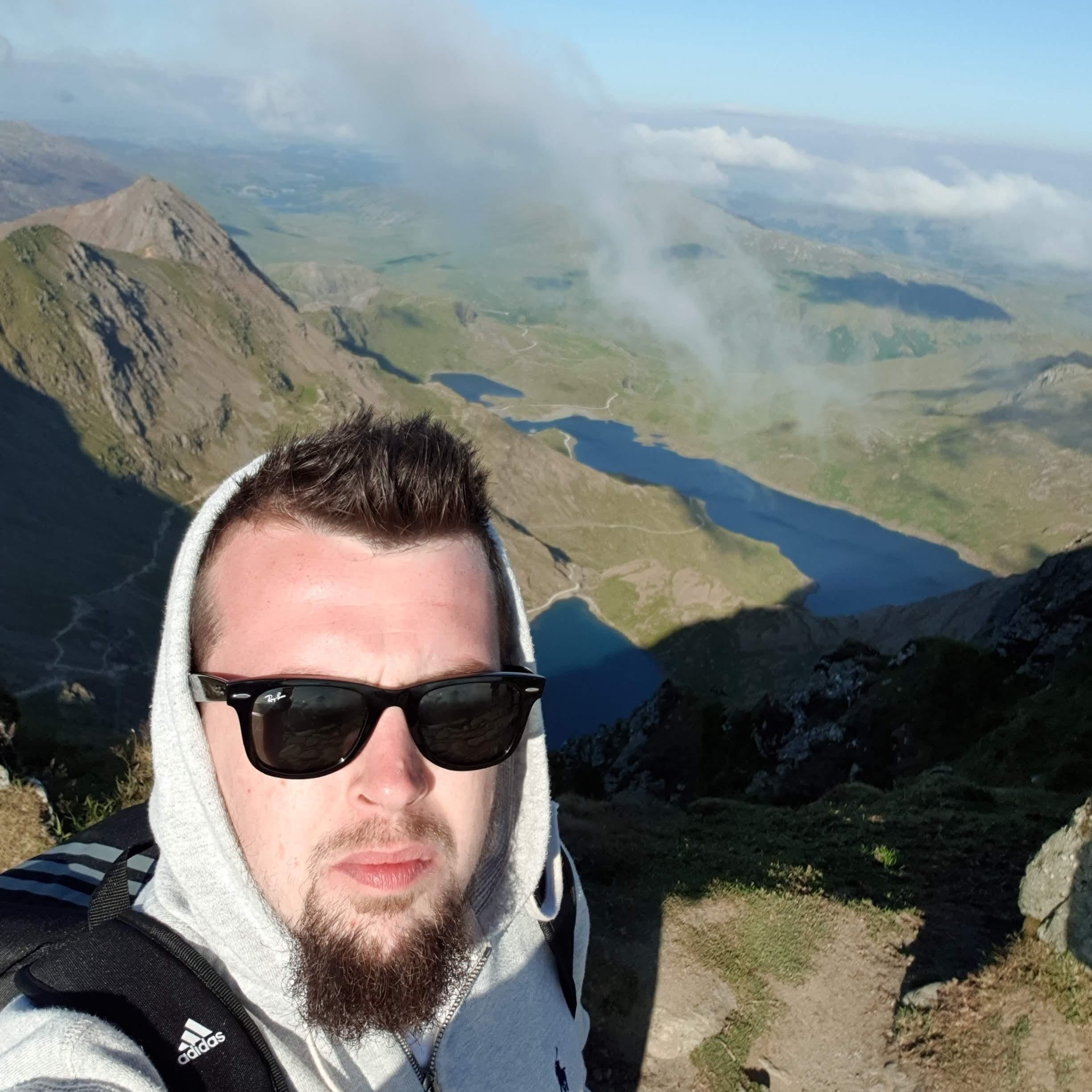 Person taking a selfie with a mountainous landscape and lake in the background